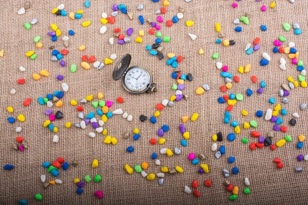 Pocket watch amid colorful pebbles on canvas background