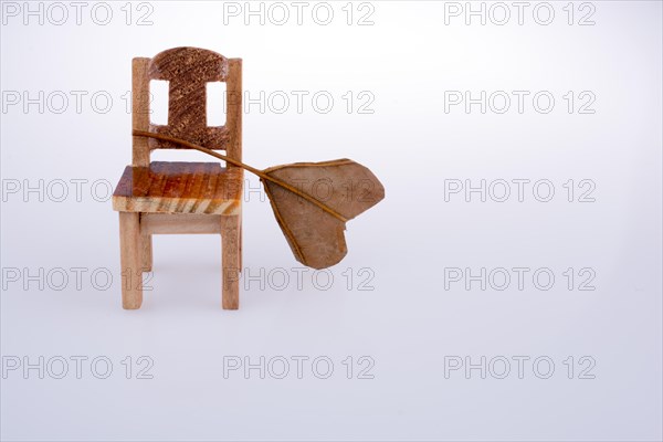 Heart shape cut dry leaf put on a little model chair on a white background