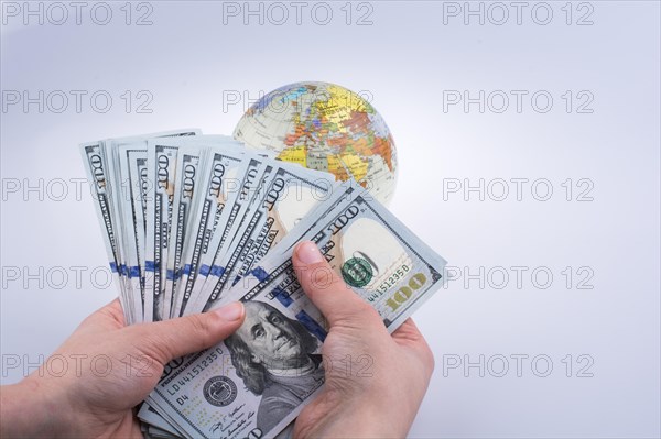 Human hand holding American dollar banknotes by the side of a model globe on white background