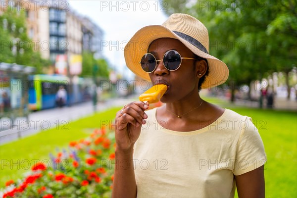 African black ethnicity woman eating a mango ice cream in the city in summer