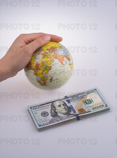 Human hand holding a model globe by the side of aAmerican dollar banknotes on white background