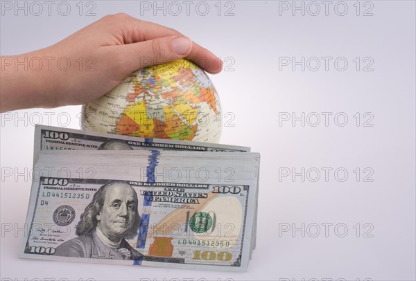 Human hand holding a model globe by the side of aAmerican dollar banknotes on white background