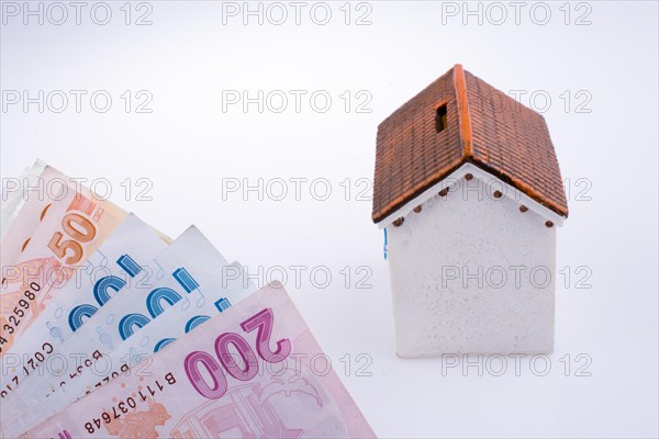 Turkish Lira banknotes by the side of a model house on white background