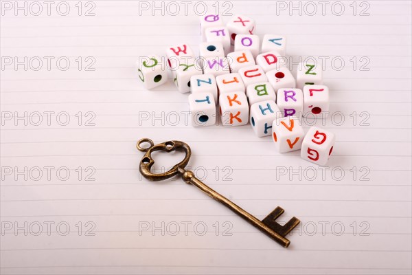 A beautiful metal key and cube letters of alphabet side by side on a sheet of paper