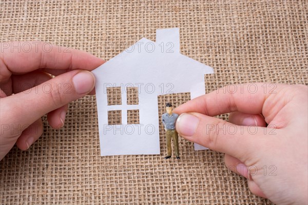 Paper house and a man figurine on a linen canvas background