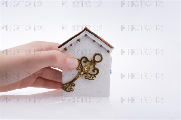 Hand holding a golden key near a house on a white background