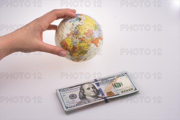 Human hand holding a model globe by the side of aAmerican dollar banknotes on white background