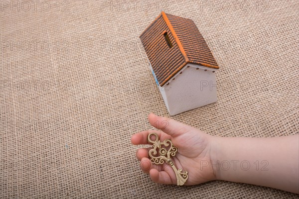 Little hand holding a retro key by a model house on a brown color background