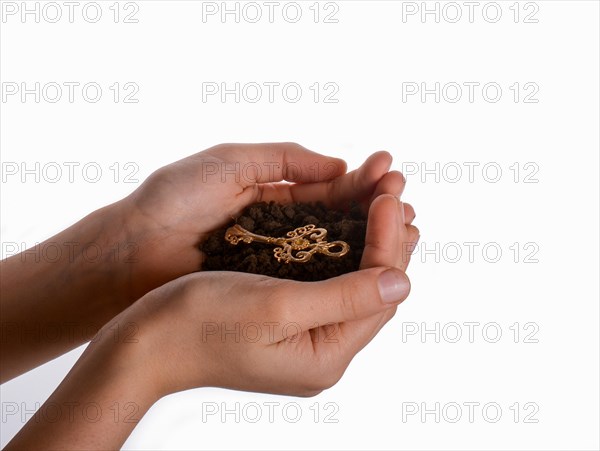 Golden key in handful soil in hand on an isolated background