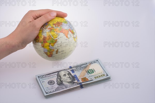 Human hand holding a model globe by the side of aAmerican dollar banknotes on white background