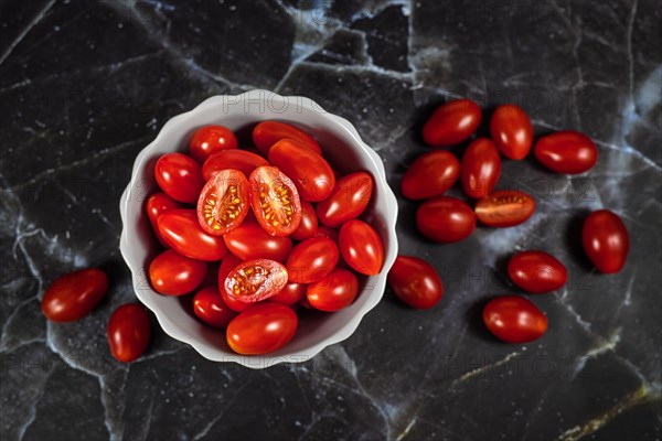 Small red ripe Roma cocktail tomatoes in white bowl on dark background