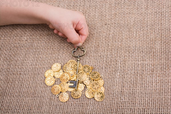 Hand holding a retro styled key over fake gold coins