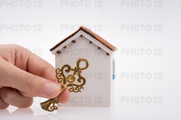 Hand holding a golden key near a house on a white background