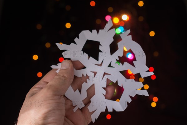 Snowflake shaped paper in hand on bokeh light background