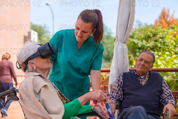 An elderly woman with the nurse looking through virtual reality glasses in the garden of a nursing home