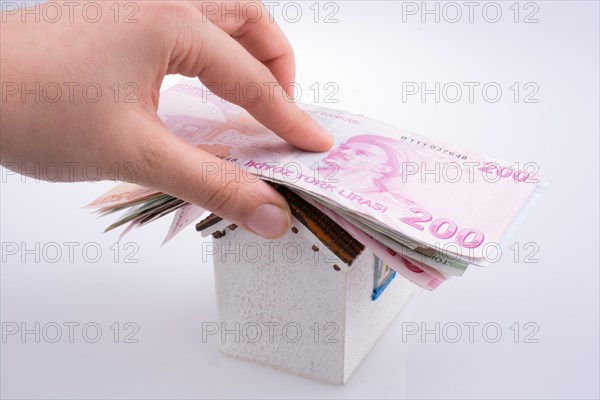 Hand holding Turkish Lira banknotes on the roof of a model house on white background