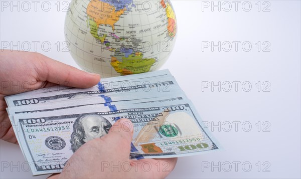 Human hand holding American dollar banknotes by the side of a model globe on white background