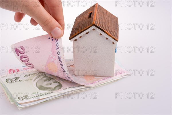 Hand holding Turkish Lira banknotes by the side of a model house on white background