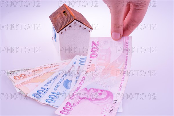 Hand holding Turkish Lira banknotes by the side of a model house on white background