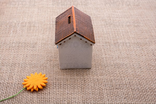 Fake flower by a model house on a brown color background