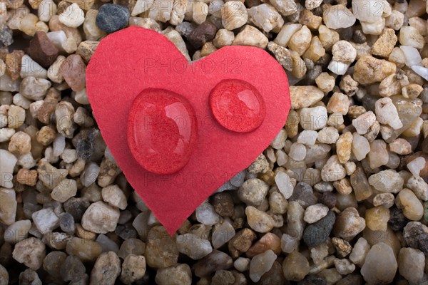 Water drops on a heart shaped paper on sand background
