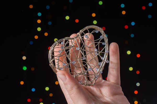 Heart shaped metal cage in hand on bokeh light background