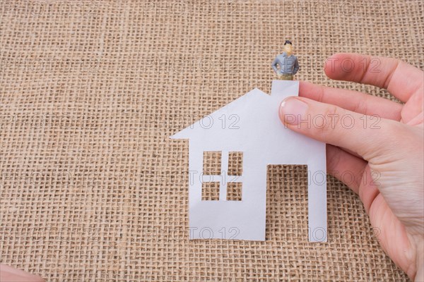 Paper house and a man figurine on a linen canvas background