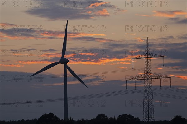 Wind power station and high voltage pylon in front of evening sky