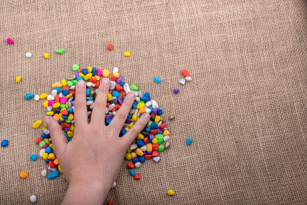 Colorful little pebbles in hand and on canvas ground