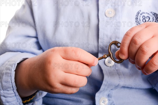 Baby with a blue shirt holding a metal key in his hand on a white background