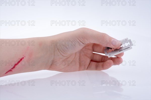Injured hand holding a razor blade on a white background