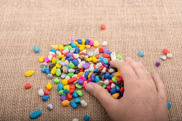 Colorful little pebbles in hand and on canvas ground