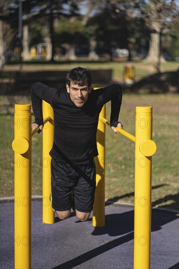 Fit young man doing push ups on horizontal bar outdoors