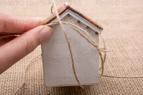 Hand holding a thread around a model house on a brown background