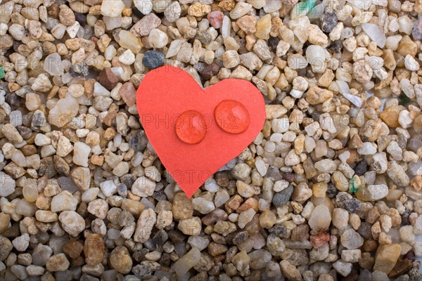 Water drops on a heart shaped paper on sand background