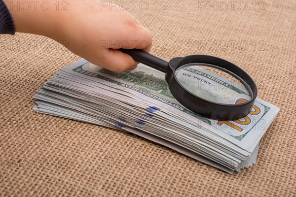 Toddler holding a magnifying glass over the banknote bundle of US dollar