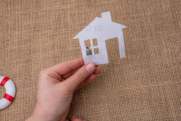 Paper house and a man figurine on a linen canvas background