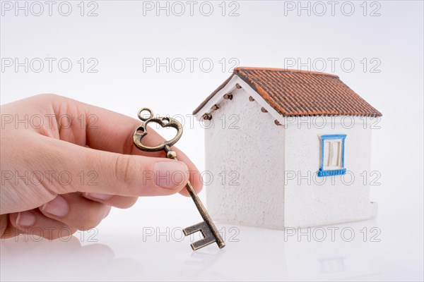 Hand holding a golden key near a house on a white background