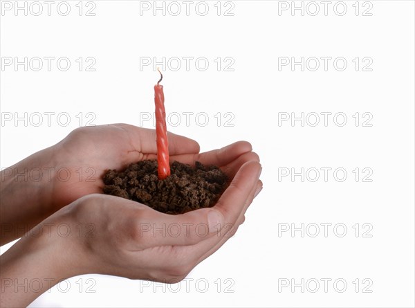 Cake candle in handful soil in hand on an isolated background