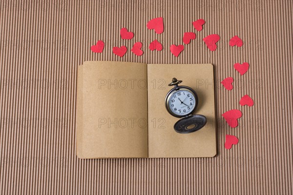 Retro Pocket watch on notebook with red paper hearts around