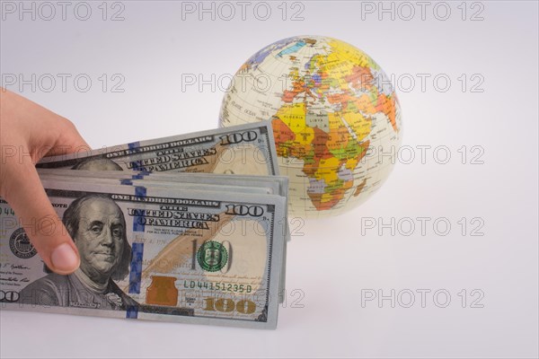 Human hand holding American dollar banknotes by the side of a model globe on white background