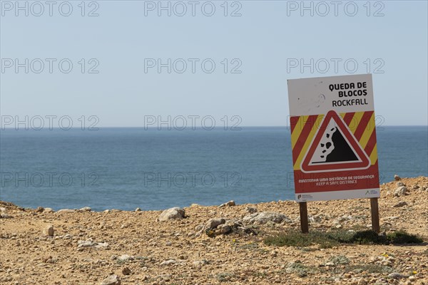 Warning sign of rockfall and falling rocks on a cliff on the rocky coast at Ponta da Sagres