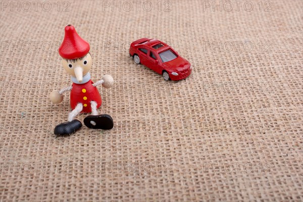 Red car and wooden Pinocchio doll sitting on canvas