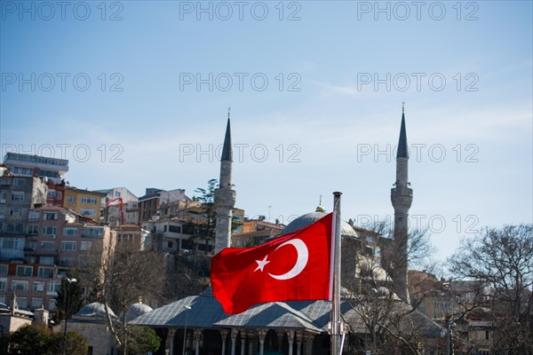 Turkish national flag hang on a pole on a rope with a minaret behind