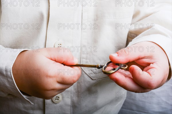 Baby's hand holding a retro styled metal key on a white background