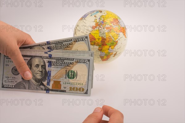 Human hand holding American dollar banknotes by the side of a model globe on white background