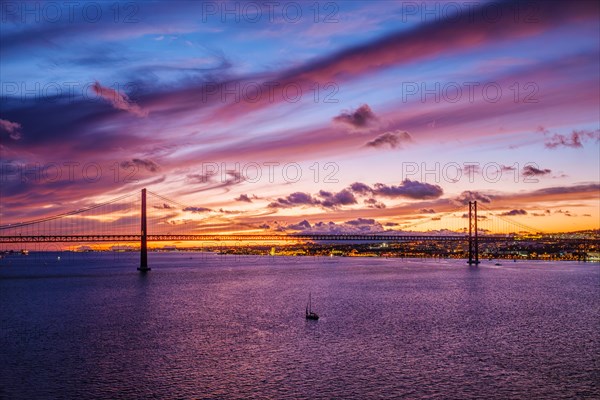 View of 25 de Abril Bridge famous tourist landmark of Lisbon connecting Lisboa and Almada on Setubal Peninsula over Tagus river in the evening twilight with boats. Lisbon