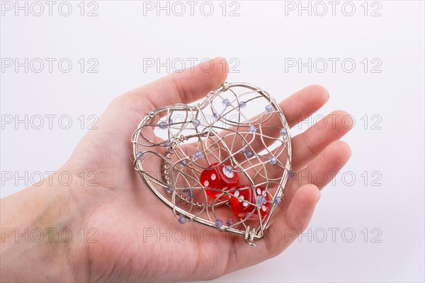 Hand holding Red dice in a heart shaped cage on a white background