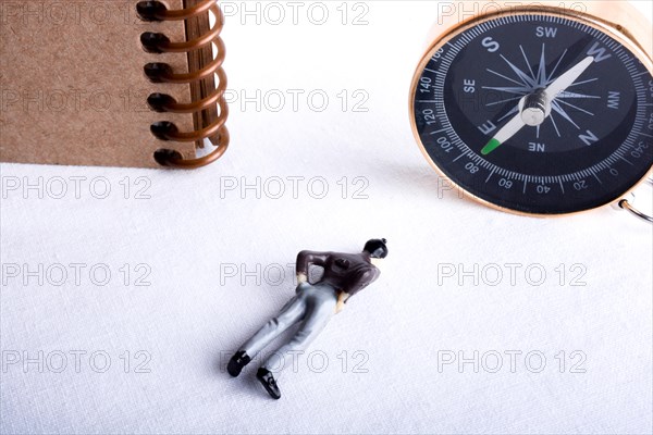Man lying down by the side of a compass and spiral notebook on a white background
