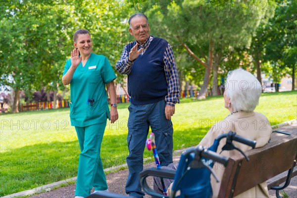 An elderly man with the nurse on a walk through the garden of a nursing home greeting an elderly woman